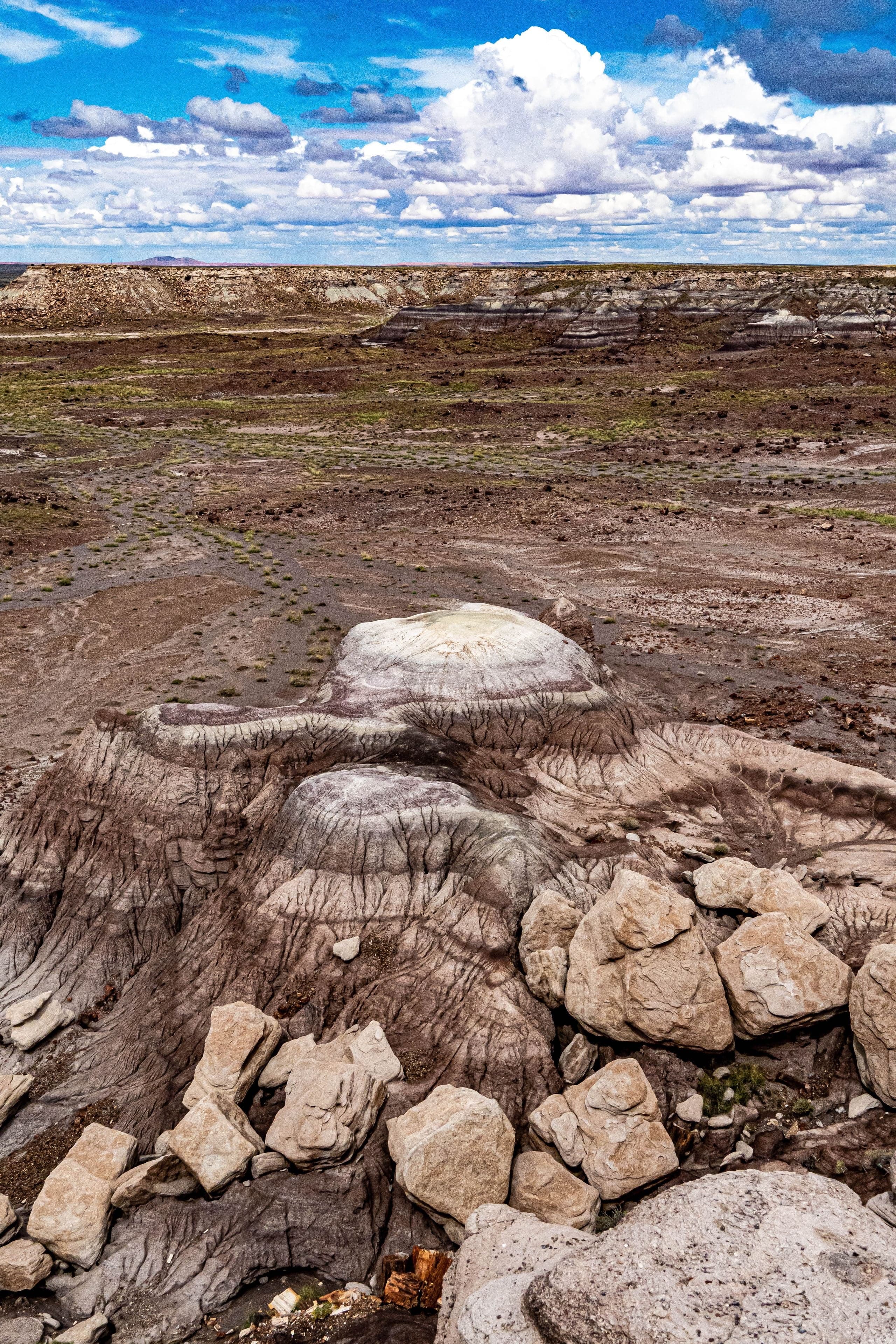 A distinctive badlands butte topped with white caprock rises from a barren eroded desert floor under bright blue sky.