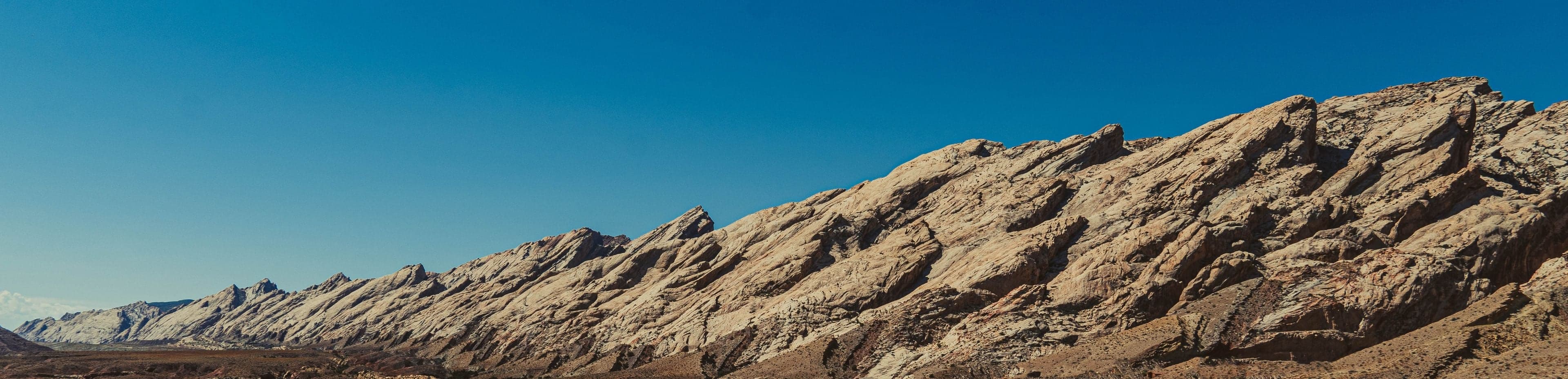 A long panorama of pale, heavily eroded folded rock ridges extending across the frame under a deep blue sky.