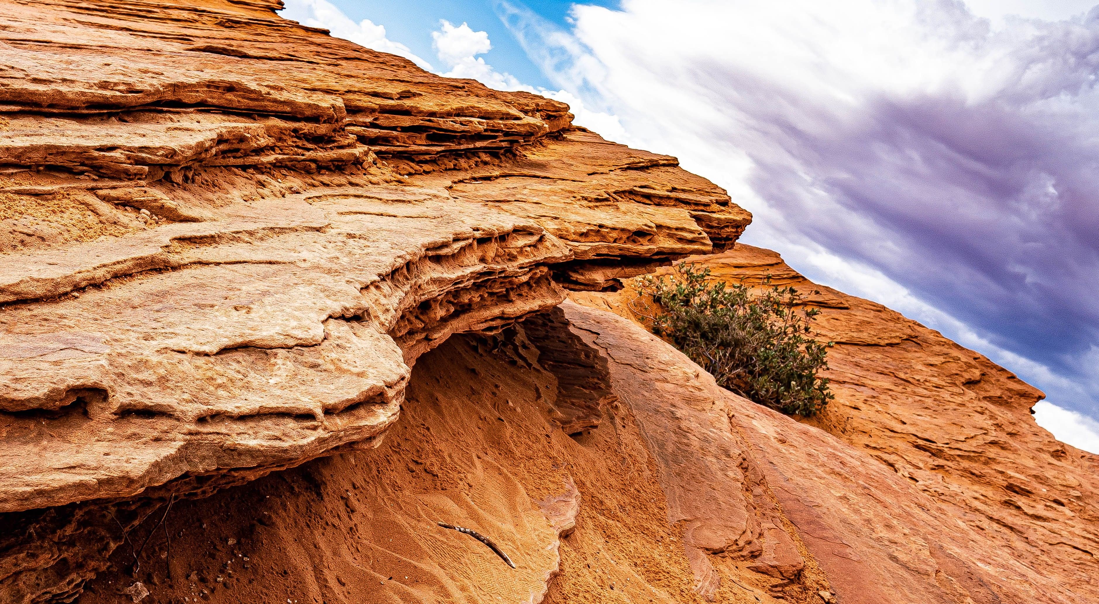 Deeply layered orange sandstone slabs angle steeply skyward against a dramatic purple and white storm sky with sparse scrub.