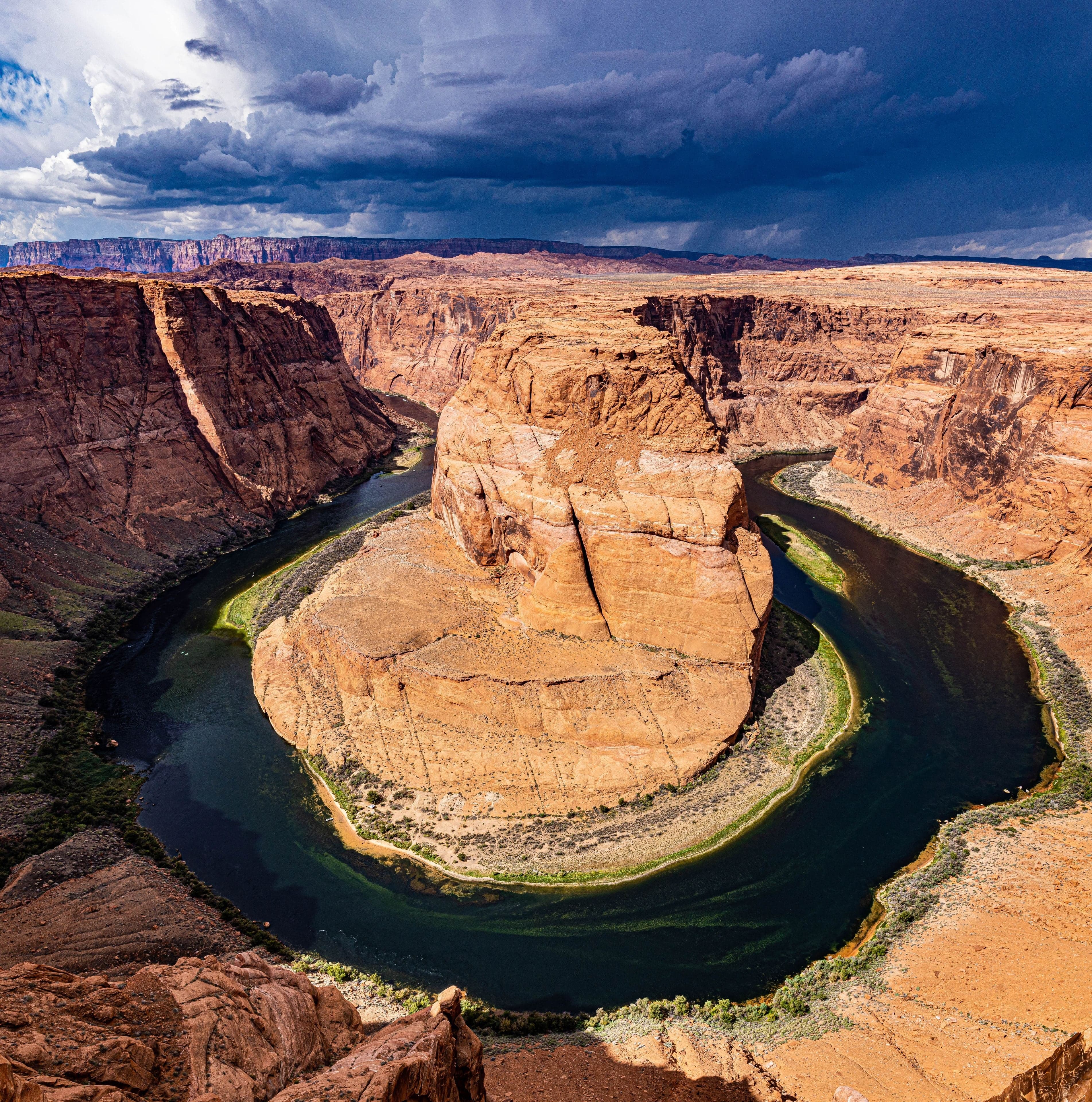 A panoramic aerial of Horseshoe Bend, the Colorado River looping through towering orange sandstone walls beneath a stormy sky.