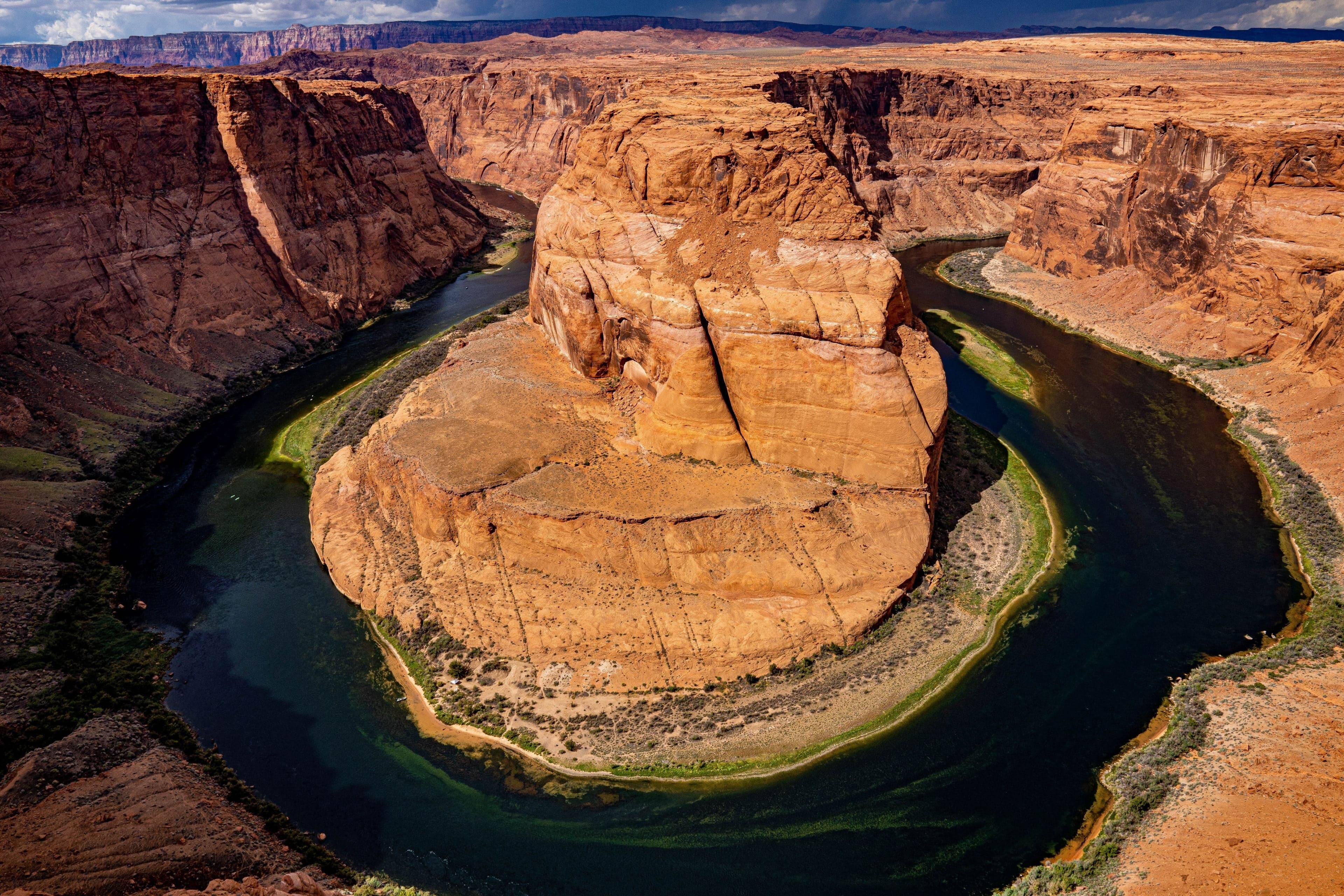 A sweeping overhead view of the Colorado River curving around a massive sandstone butte at Horseshoe Bend under a moody storm sky.