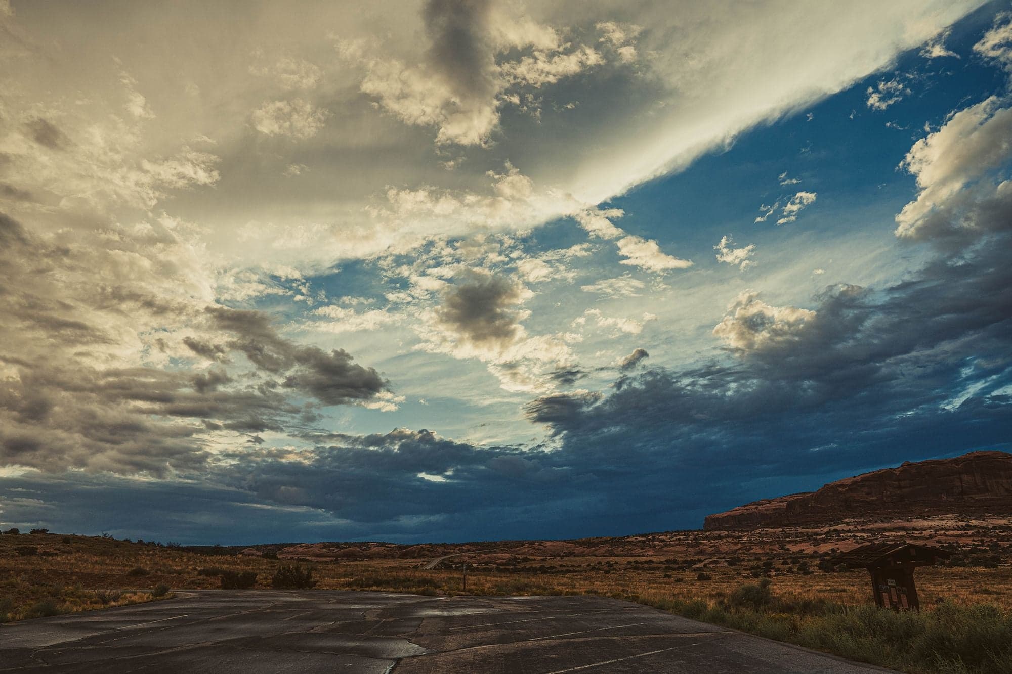 A black Ram 3500 truck parked on a desert road with a gray wolfdog in the window, red mesas and storm clouds behind.