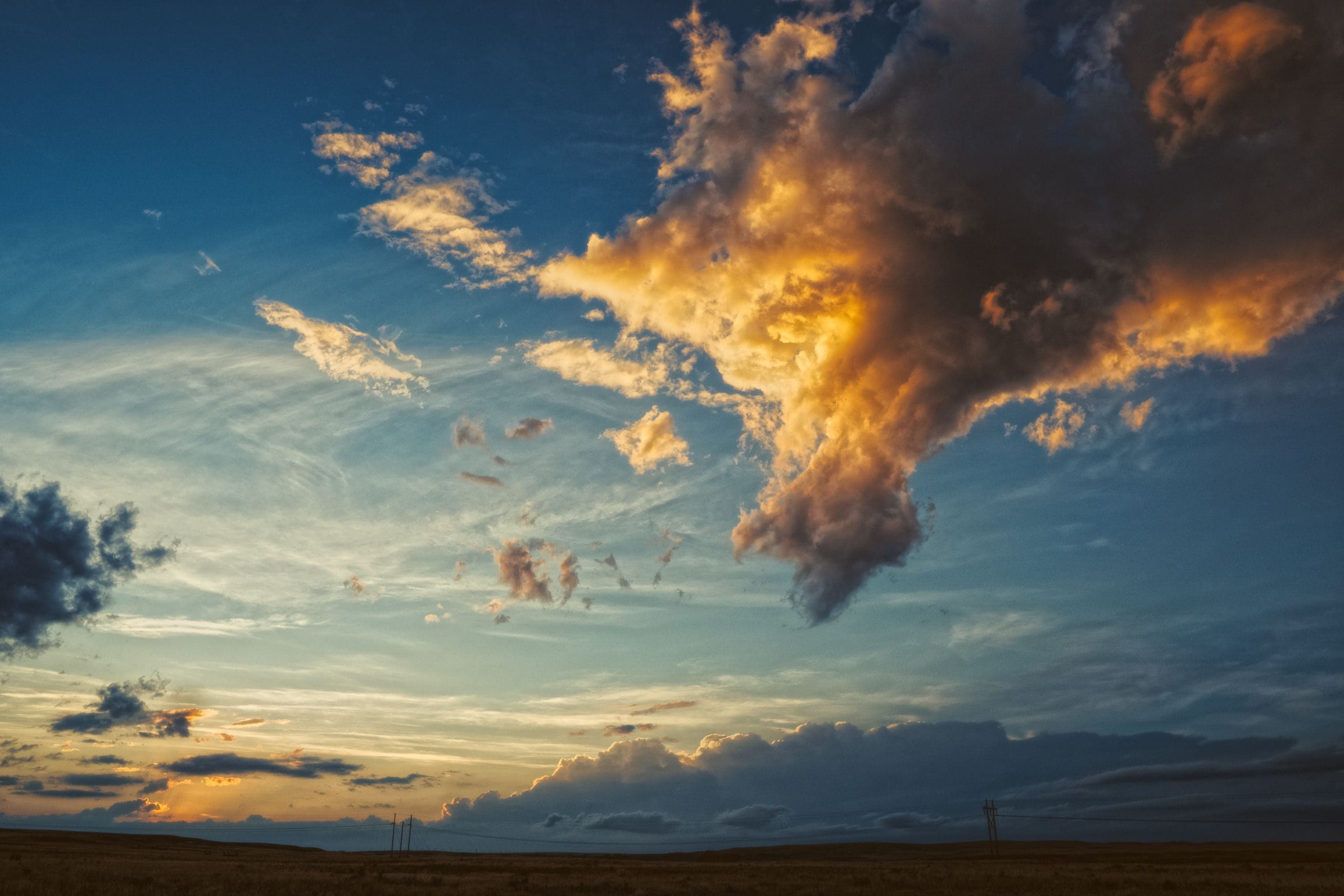 A dramatic sunset sky over a flat Wyoming plain with a massive cumulonimbus lit vivid orange-gold against deep blue.