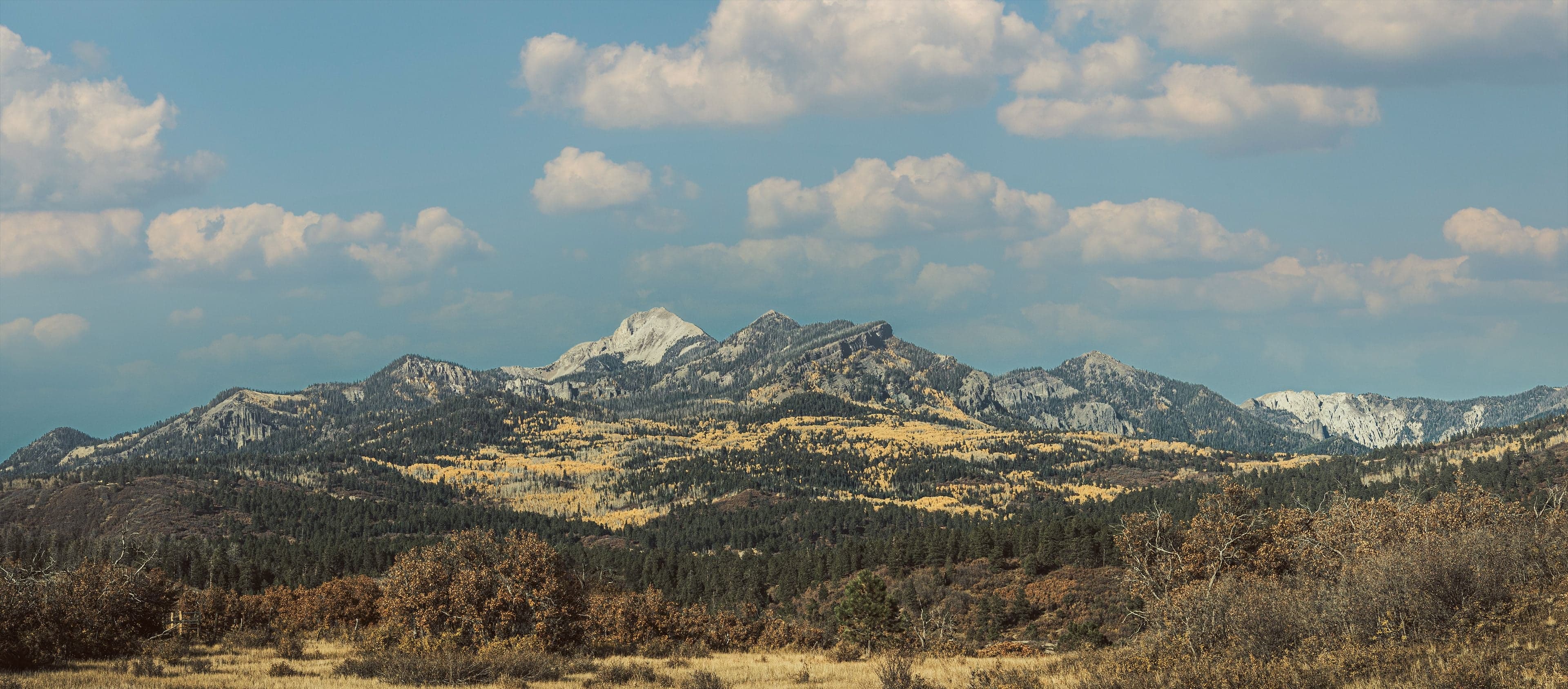 A wide panorama of a rugged Colorado range near Pagosa Springs in autumn under a partly cloudy blue sky.