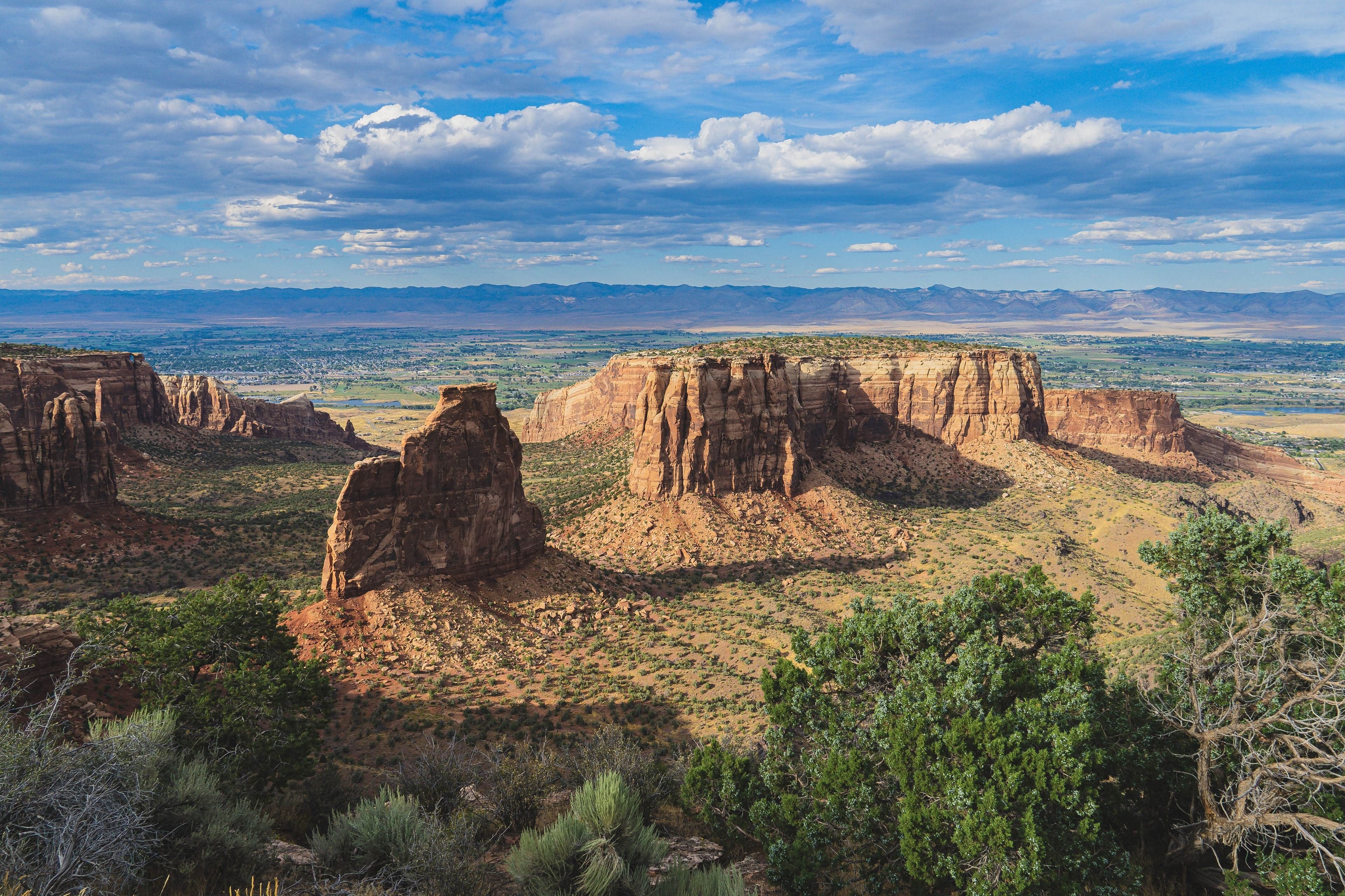 Two large sandstone buttes and a flat-topped mesa fill the frame under a cloud-dotted sky above the Colorado River valley.