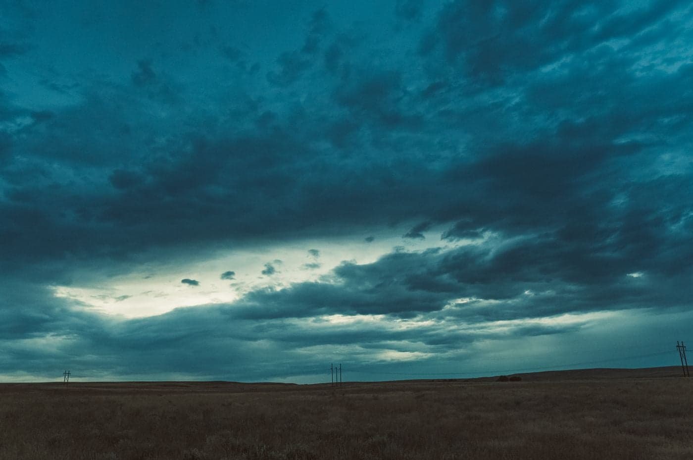 A moody flat Wyoming grassland under a heavy dark blue storm sky with layered clouds and distant utility poles.